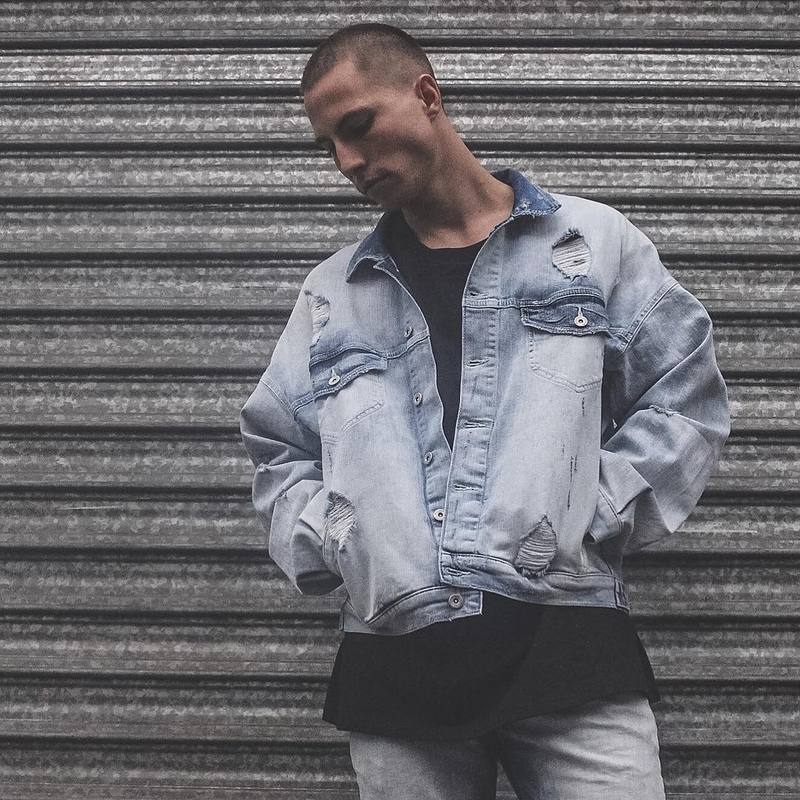 Man wearing a light blue denim jacket with visible wear against a metallic shutter background