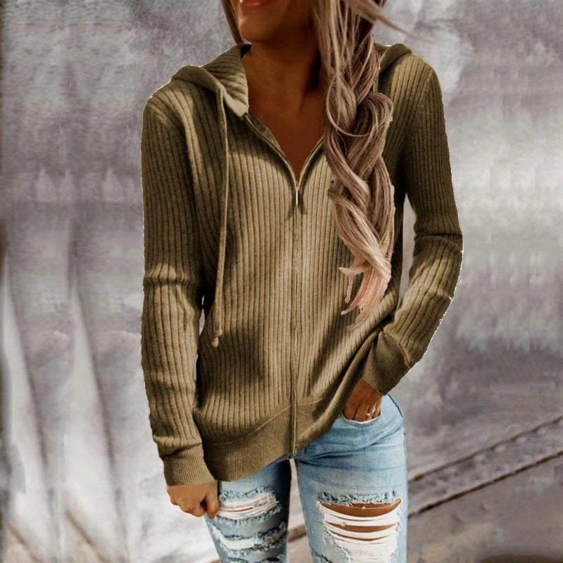 Person wearing a ribbed brown hoodie and ripped jeans against a neutral background
