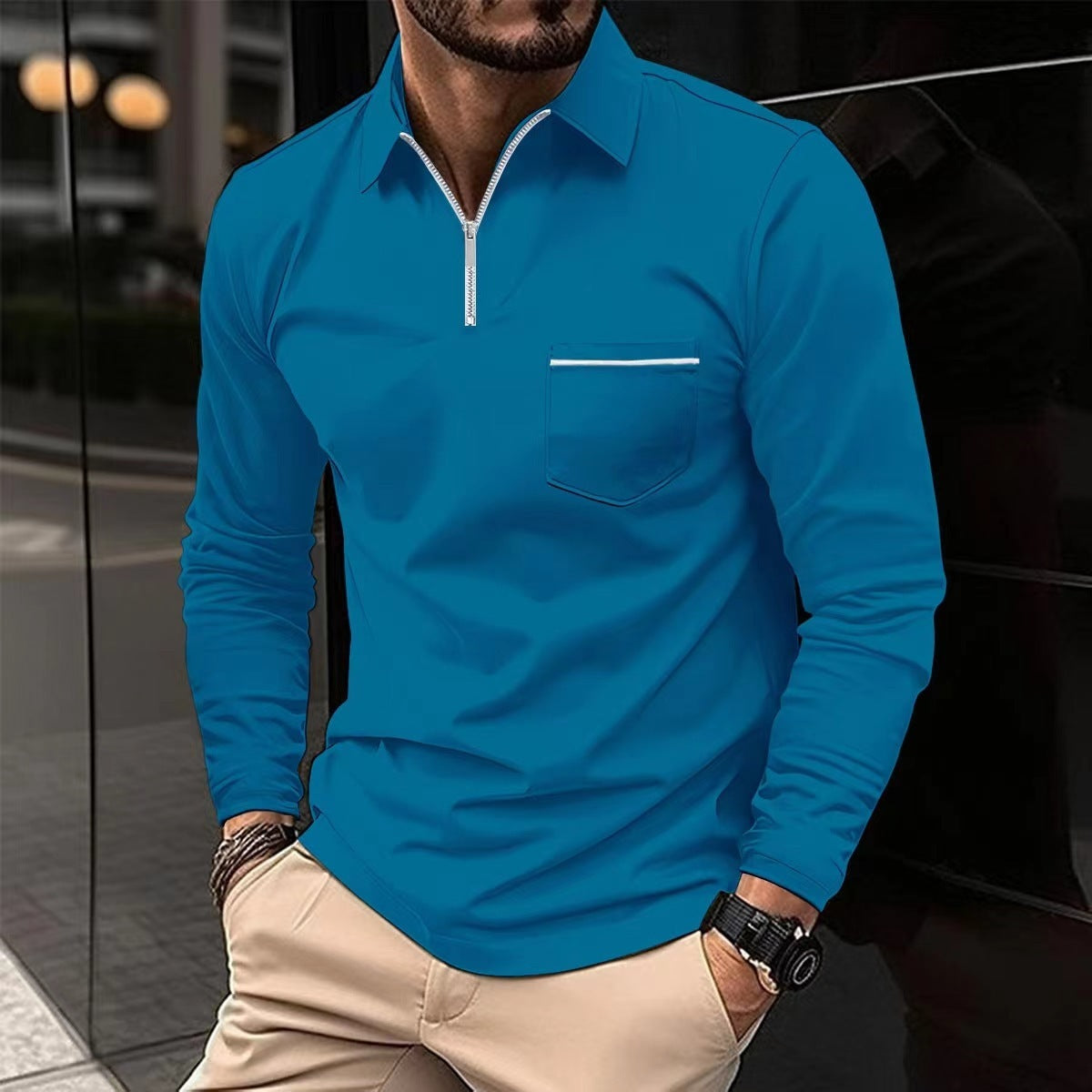 Man wearing a blue long-sleeve shirt with a zipper and pocket, standing against a reflective surface.