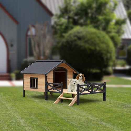 Two dogs on a wooden doghouse with a black roof in a grassy area.