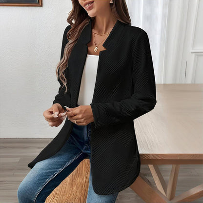 Woman wearing a black blazer over a white top and blue jeans, sitting on a wooden bench.
