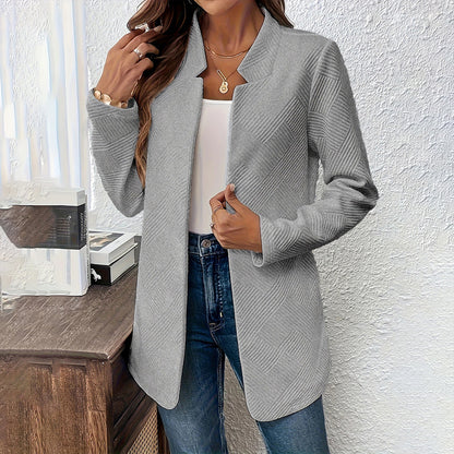 Woman wearing a gray cardigan over a white top and blue jeans against a white wall.