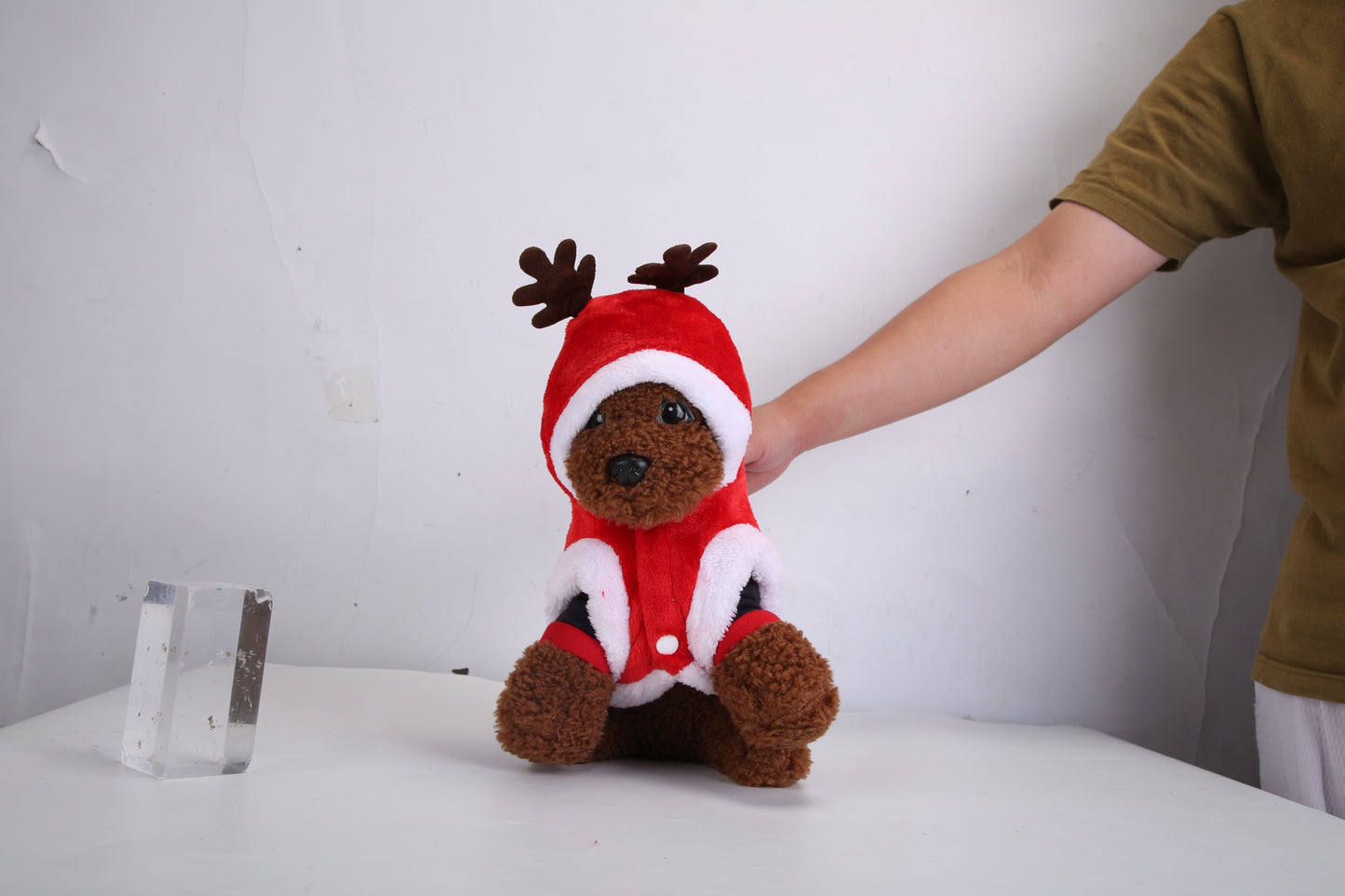 Stuffed reindeer toy with a person's hand holding it on a white surface.