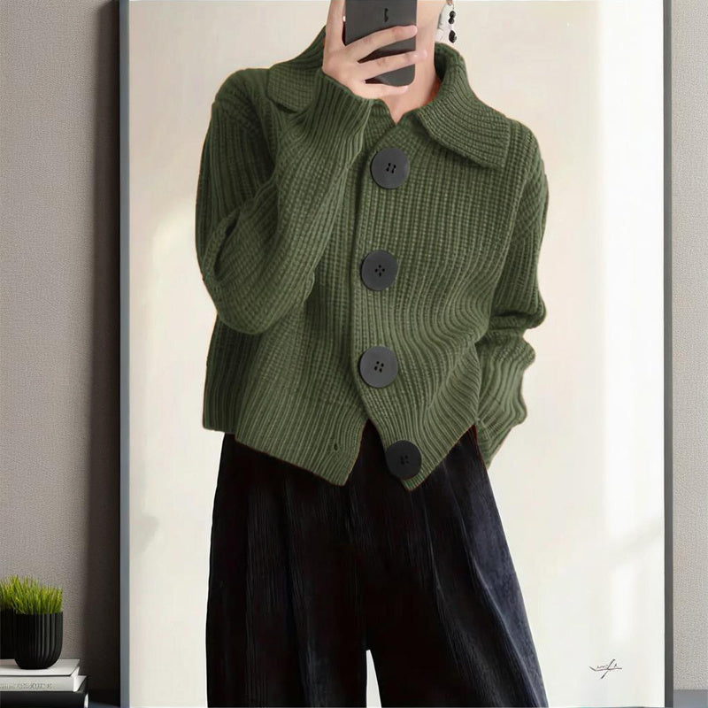 Person wearing a green knitted cardigan with black buttons in front of a mirror.