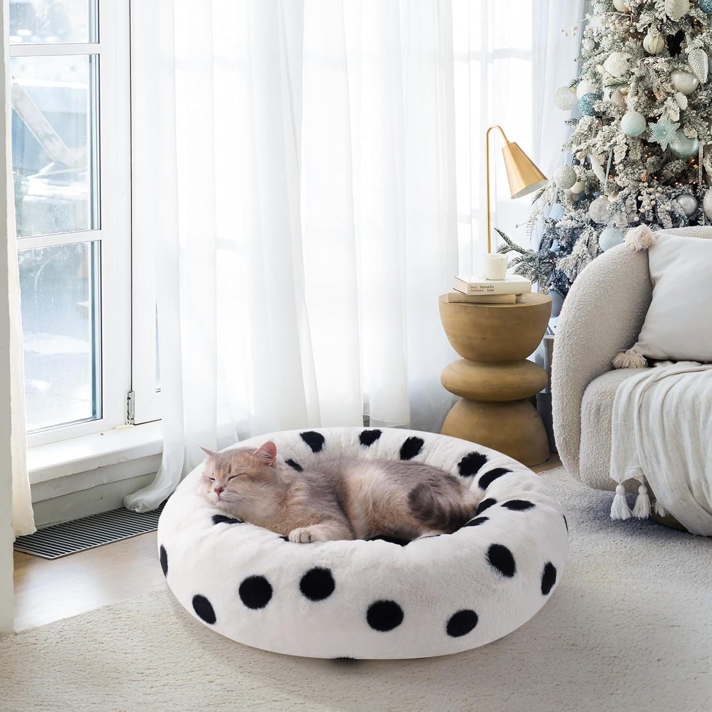 Cat lying on a polka dot bed in a cozy living room with a Christmas tree.