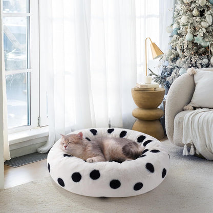 Cat lying on a polka dot bed in a cozy living room with a Christmas tree.