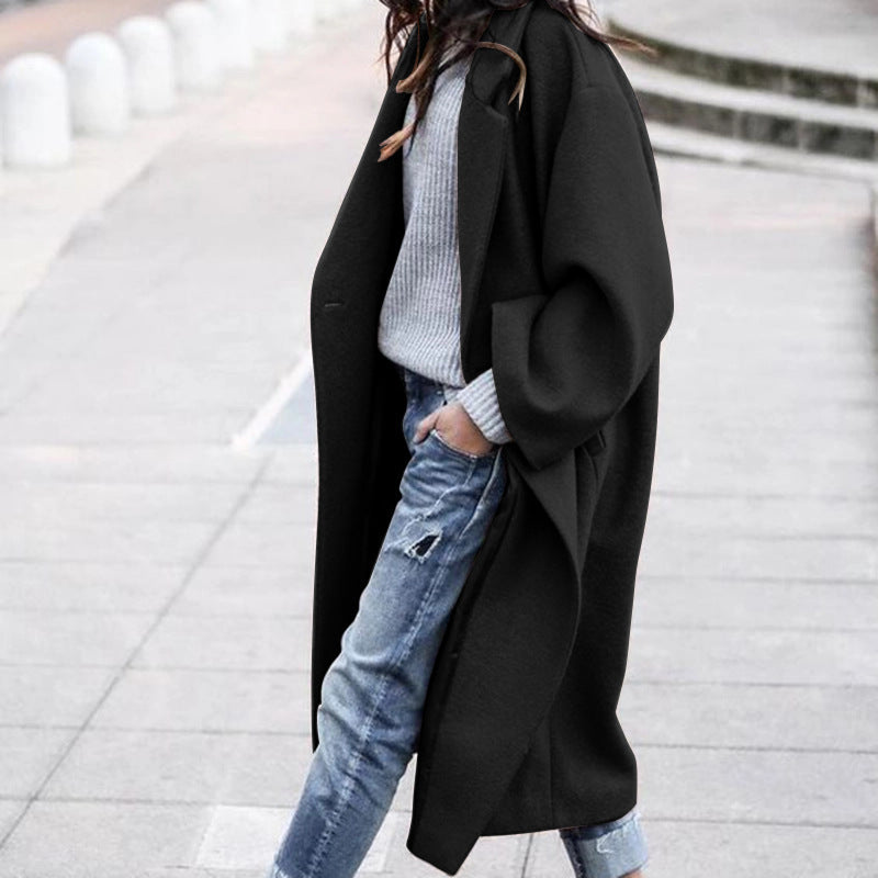 Person wearing a black coat over a light gray sweater and blue jeans on a city street.