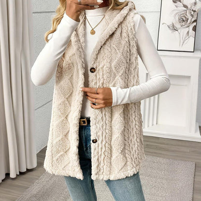 Person wearing a cream-colored cable knit vest over a white long-sleeve shirt and jeans, standing in a room with a neutral decor.