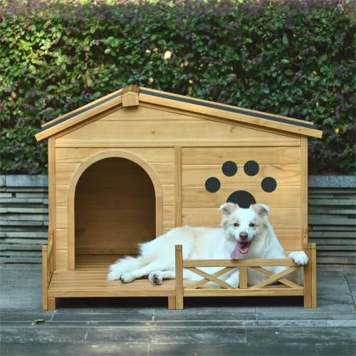 Dog sitting in a wooden doghouse with a black paw print design, surrounded by greenery.