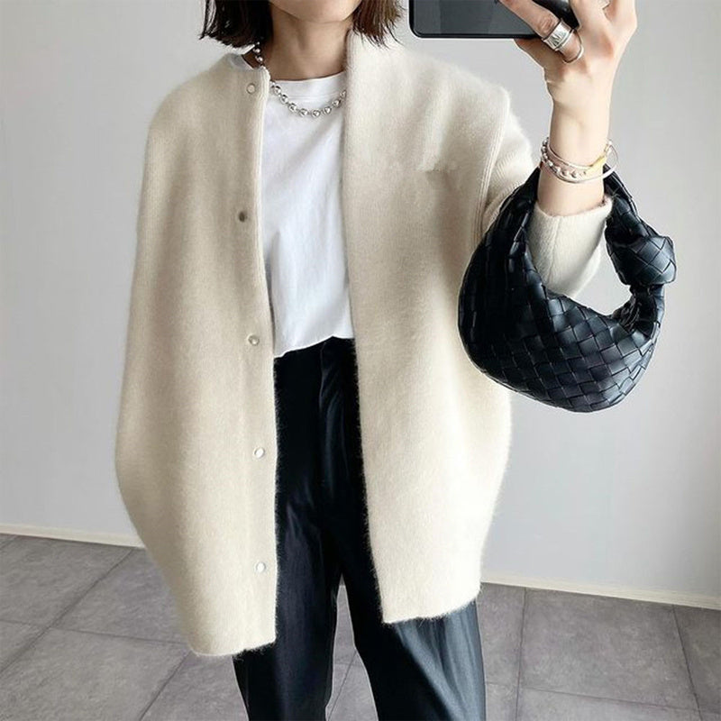 Person wearing a beige cardigan, white shirt, black pants, and holding a black handbag.