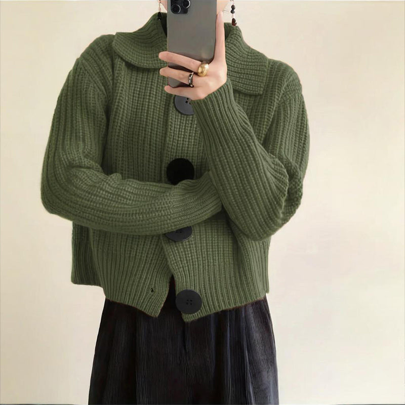 Person wearing a green knitted cardigan with black buttons against a plain background