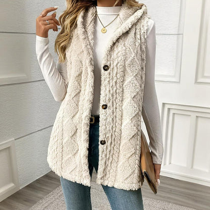 Person wearing a cream-colored cable knit vest with buttons, holding a clutch.