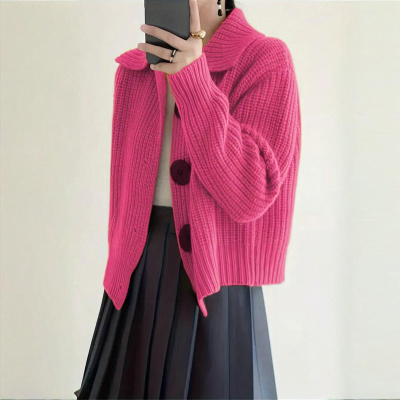 Person wearing a bright pink knitted cardigan with black heart patterns on a plain background