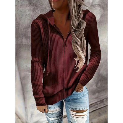 Woman wearing a ribbed burgundy hoodie with a zipper, paired with distressed jeans on a neutral background.