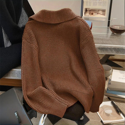 Brown sweater draped over a chair in an indoor setting with books and a cup on a table.