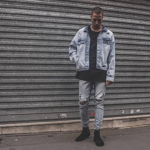 Person wearing a light blue denim jacket and jeans standing in front of a metal shutter.