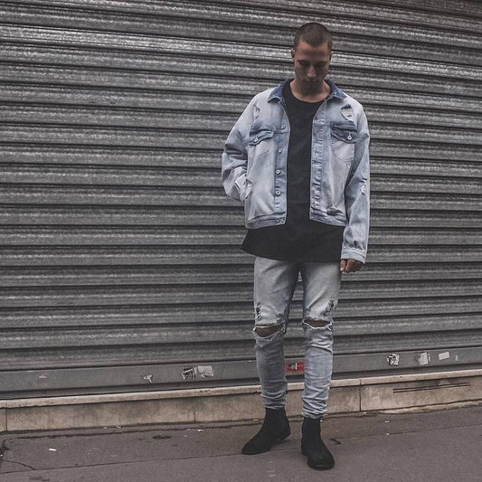 Person wearing a light blue denim jacket and jeans standing in front of a metal shutter.