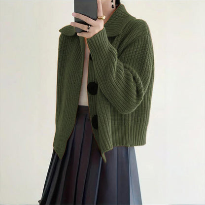 Person wearing a green knitted cardigan with black buttons on a plain background