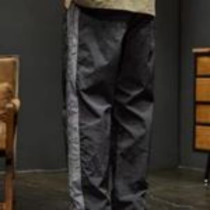 Person wearing black pants with a stripe in a room with a chair and lamp.