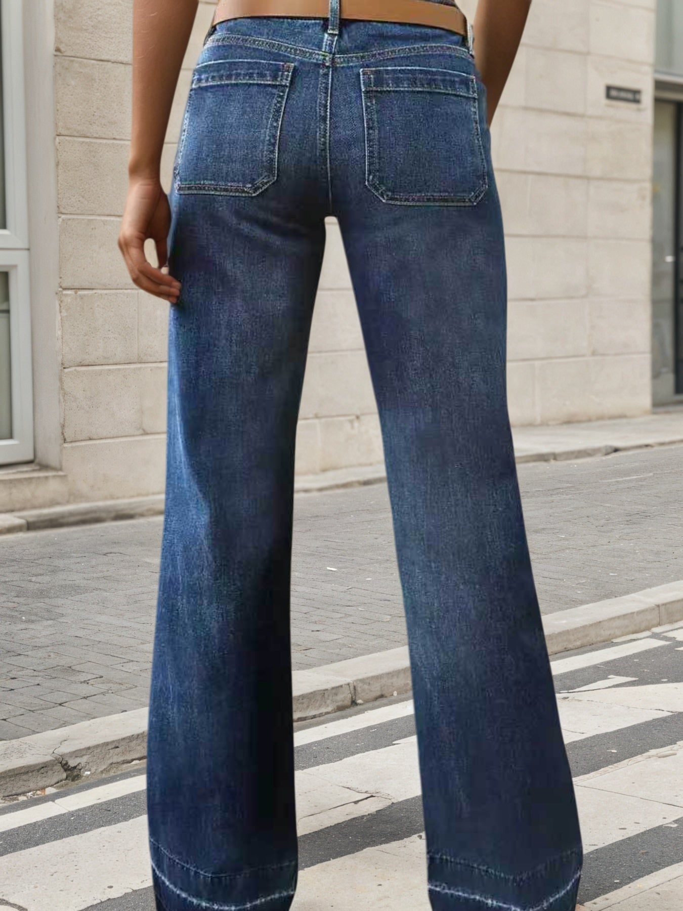 Person wearing blue flared jeans standing on a street with a building in the background