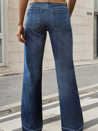 Person wearing blue flared jeans standing on a street with a building in the background