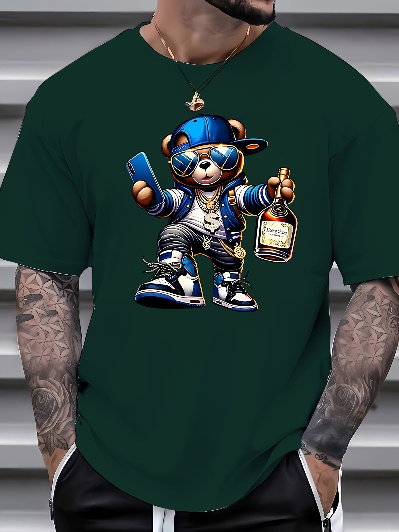 Green t-shirt with a bear graphic holding a bottle and phone, worn by a person with tattoos.