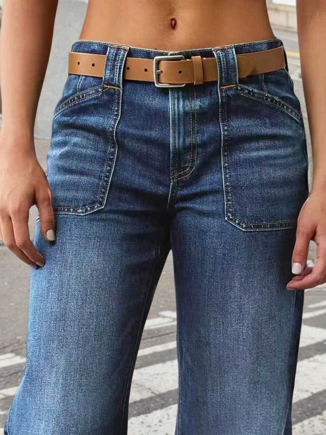 Person wearing blue jeans with a brown belt on a street background