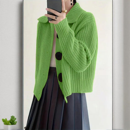 Person wearing a bright green knitted cardigan with black buttons, standing against a neutral background.