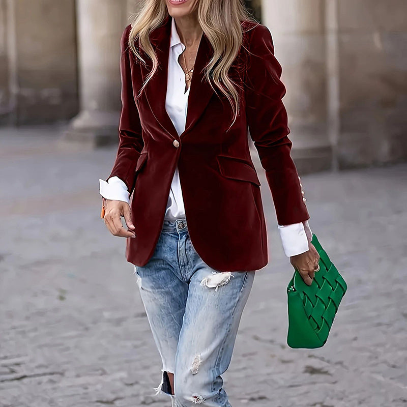 Woman wearing a red blazer, white shirt, and blue jeans, holding a green clutch.