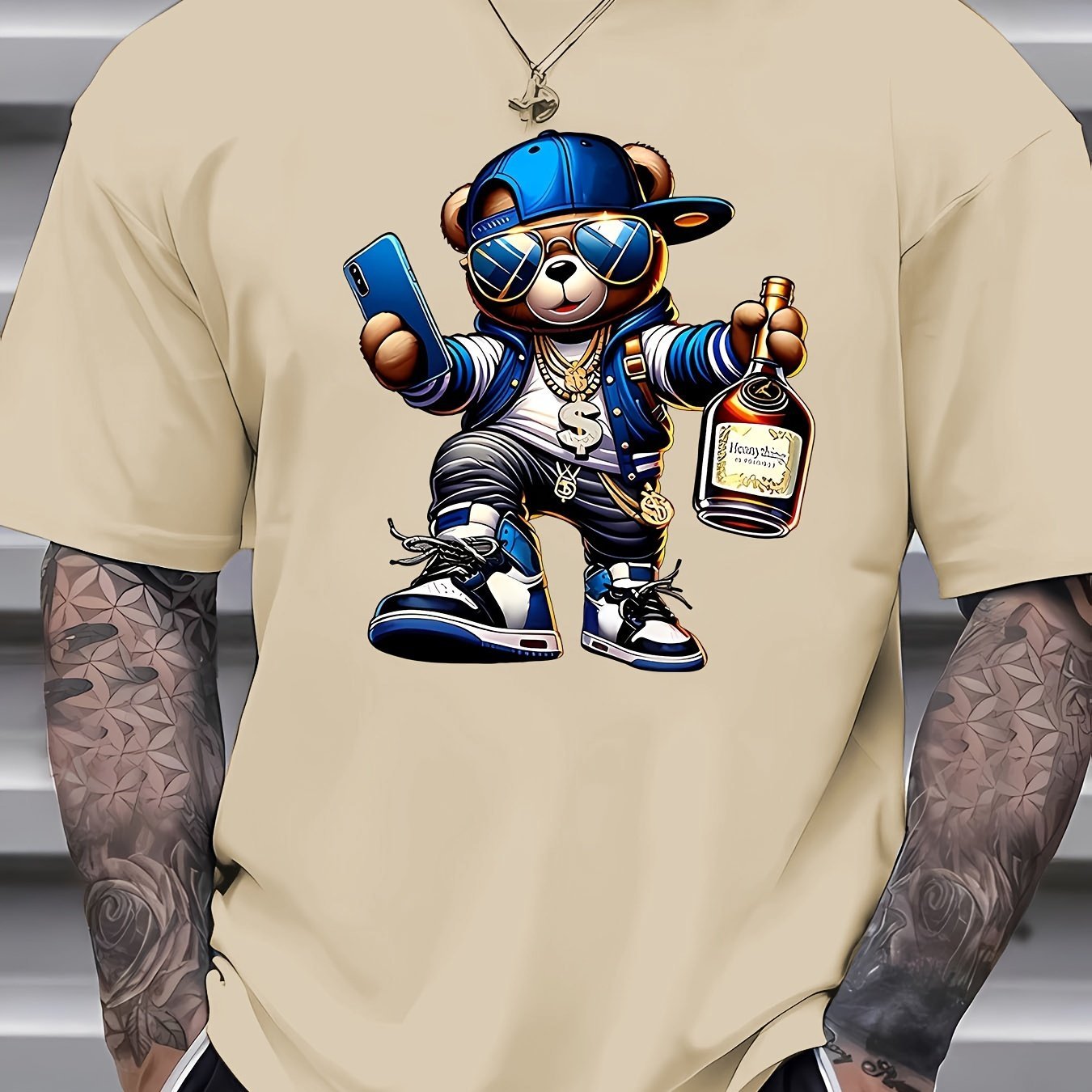 Beige t-shirt with a cartoon bear holding a phone and bottle, worn by a person with tattoos.