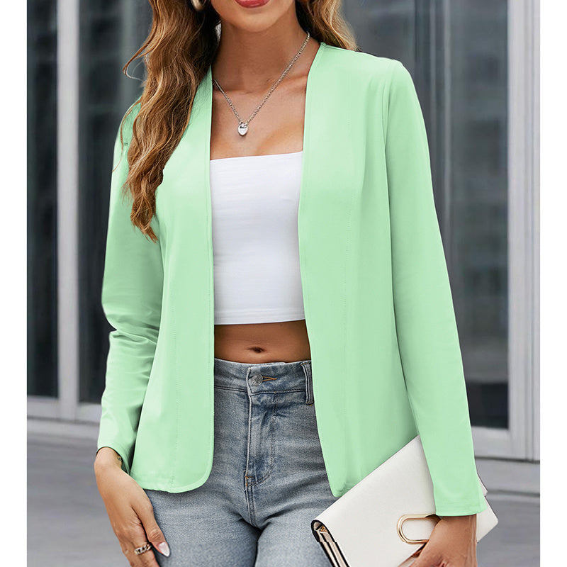 Woman wearing a light green blazer over a white top and blue jeans, holding a clutch.