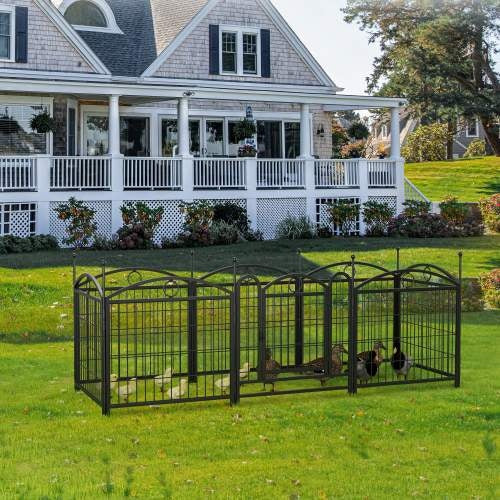 Large metal pet pen with ducks on a grassy lawn in front of a house.