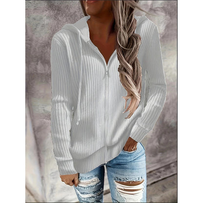 Woman wearing a white ribbed sweater and ripped jeans against a neutral background