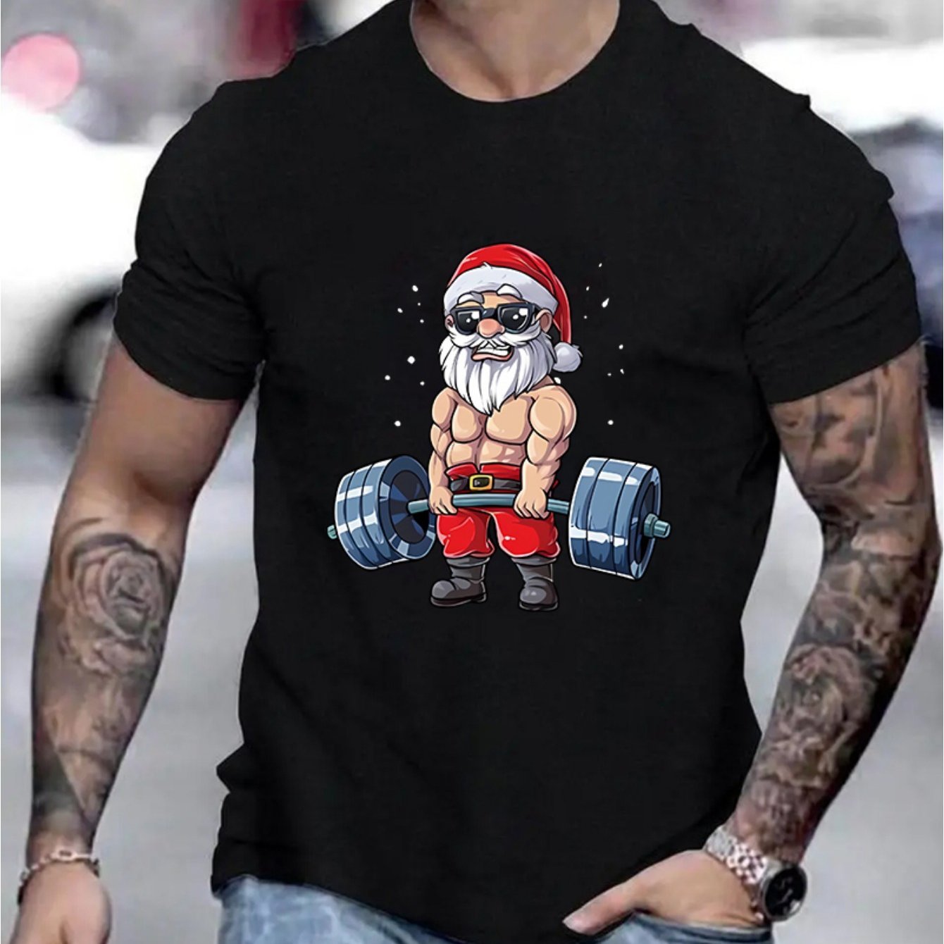 Black t-shirt with a graphic of Santa Claus lifting weights, worn by a person with tattoos.