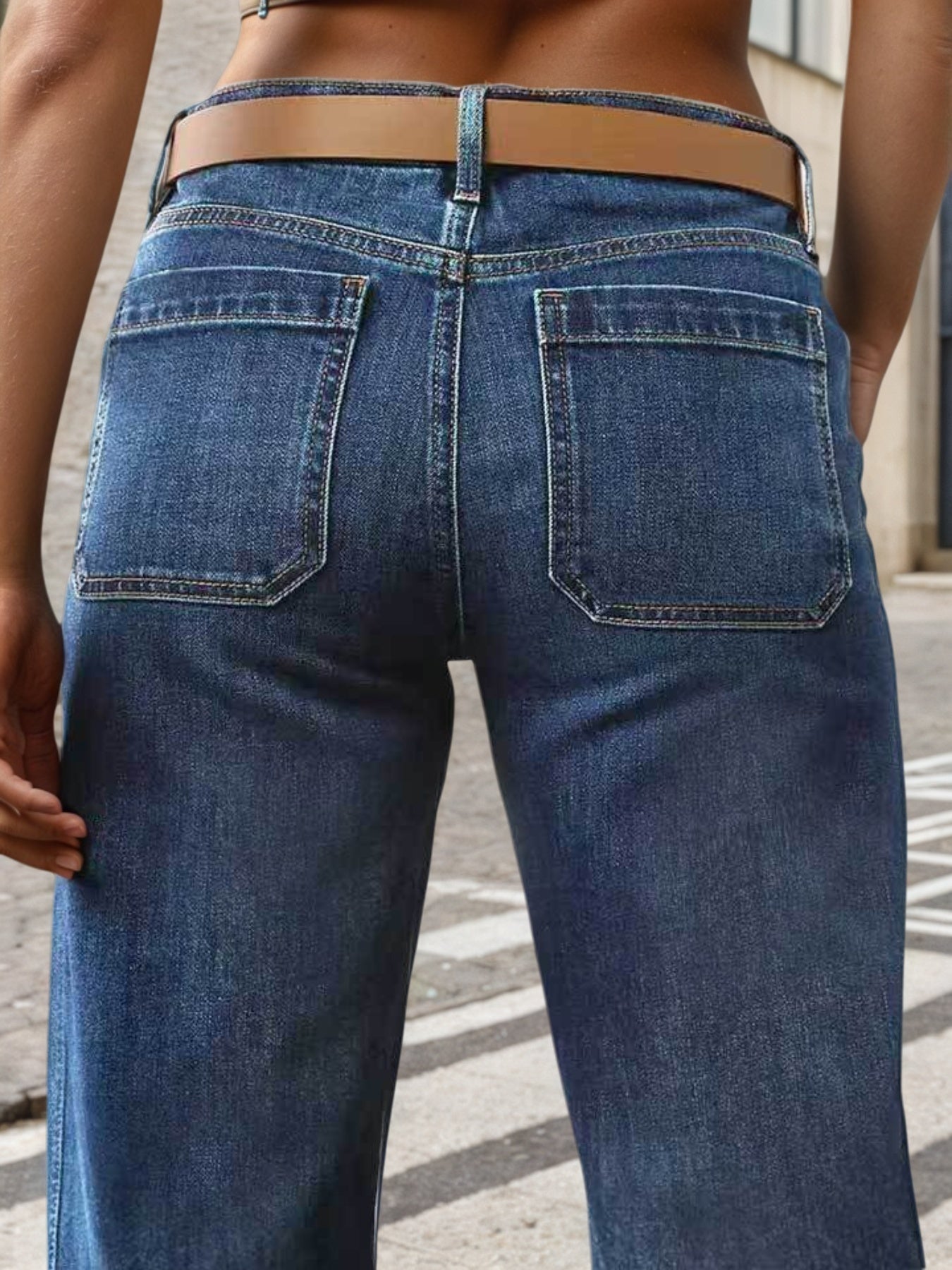 Person wearing blue jeans with a brown belt on a street.