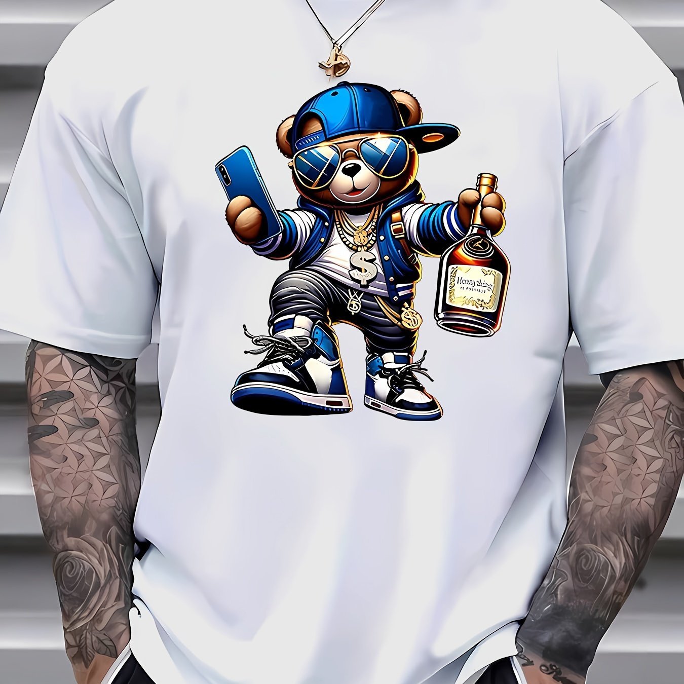 White t-shirt with a cartoon bear design holding a phone and bottle, worn by a person with tattoos.
