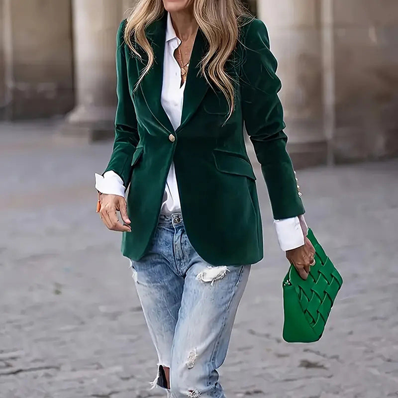 Person wearing a green blazer, white shirt, and blue jeans, holding a green handbag.