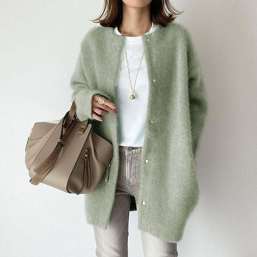 Person wearing a light green cardigan holding a beige handbag against a plain background